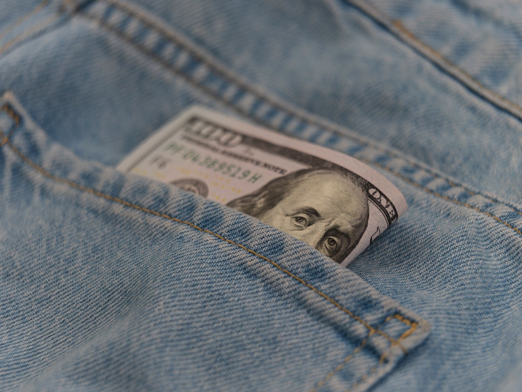 Close-up of a 100 dollar bill in a denim pocket, symbolizing finance and savings.