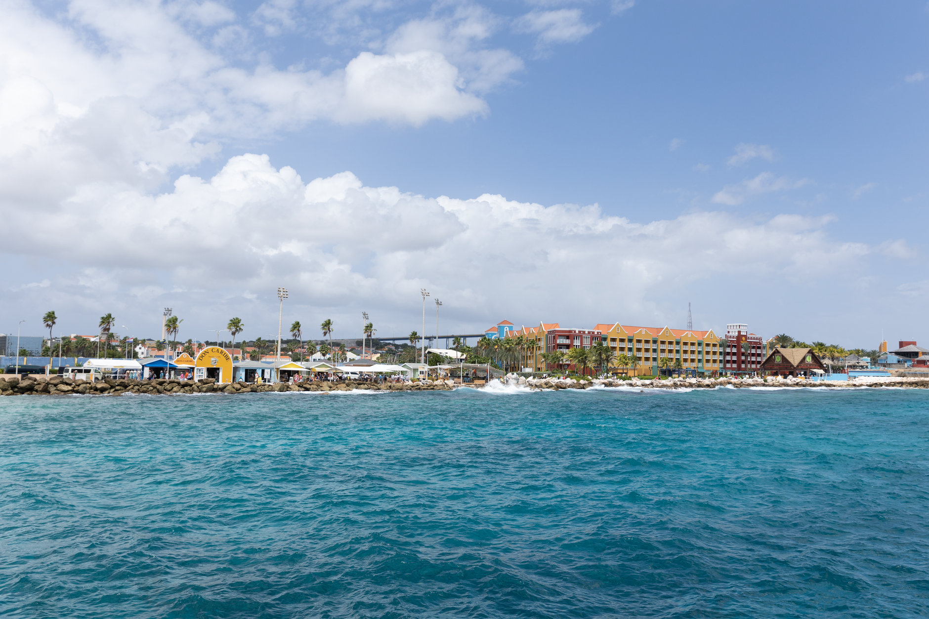 Panoramic view of a colorful tropical resort along a crystal-clear seaside under a bright sky.