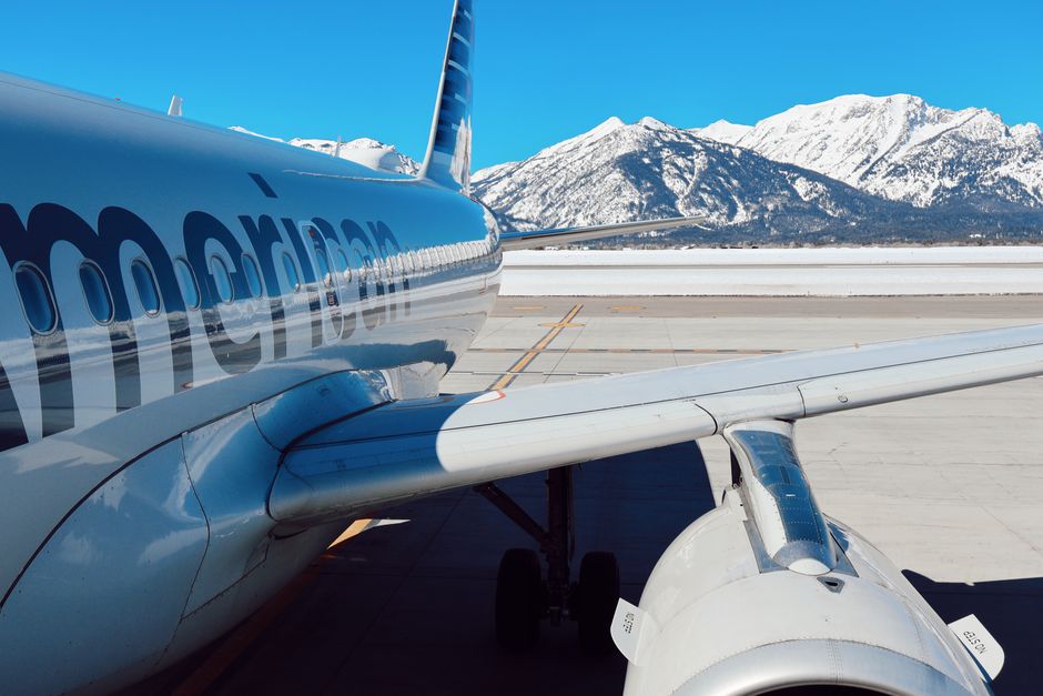 An airplane parked on the runway with snowy mountains in Jackson, WY, under a clear blue sky.