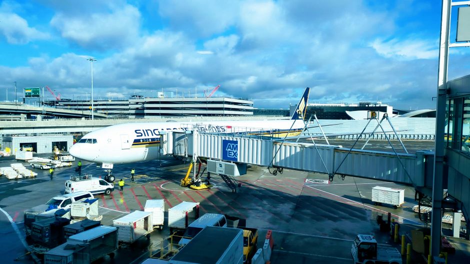 Singapore Airlines Boeing 777 at JFK Airport gate with jet bridge and ground support equipment.