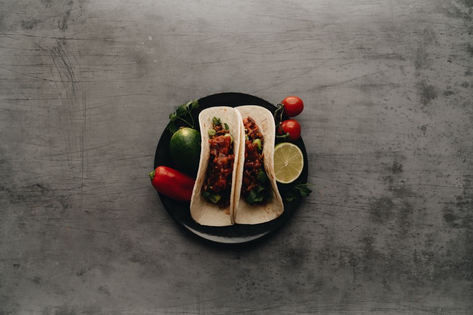 Delicious tacos with fresh cherry tomatoes, lime, and pepper on a plate, perfect for a Mexican-themed meal.