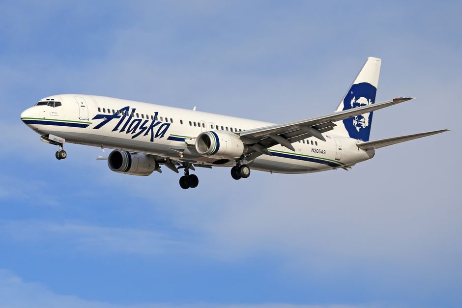Alaska Airlines Boeing jet soaring through a clear blue sky.