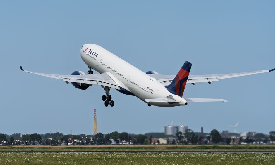 Delta Air Lines airplane taking off against a clear blue sky with cityscape background.