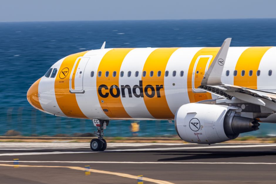 A Condor Airlines plane takes off from a sunny coastal airport in Spain.