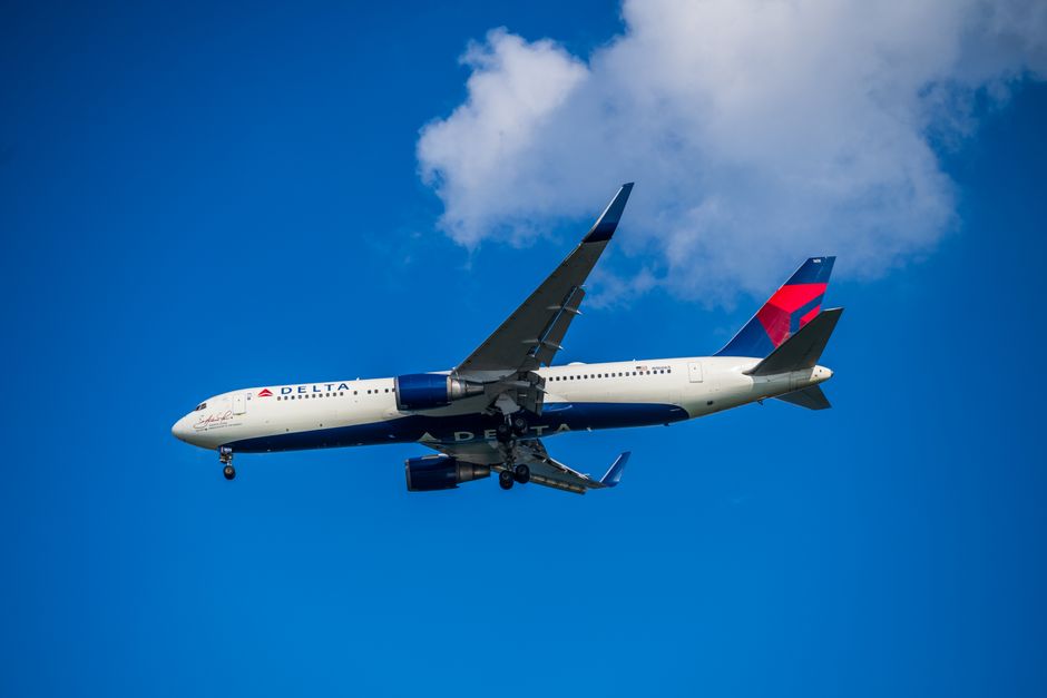 A Delta Air Lines plane flying in a clear sky with slight clouds, showcasing aviation and travel