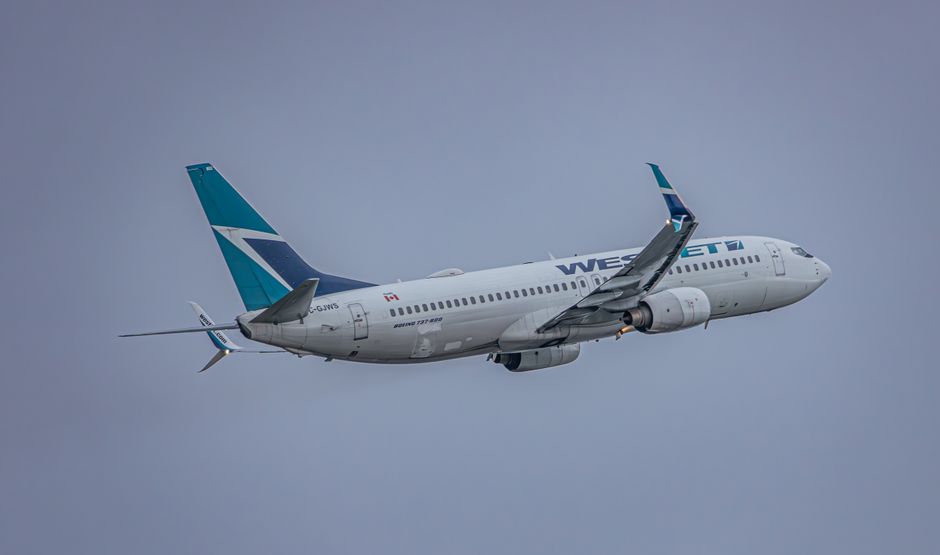 A WestJet airplane captured mid-flight against a cloudy sky, showcasing modern aviation.