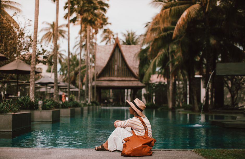 Side view full body calm female in maxi dress and summer hat resting on poolside in tropical resort