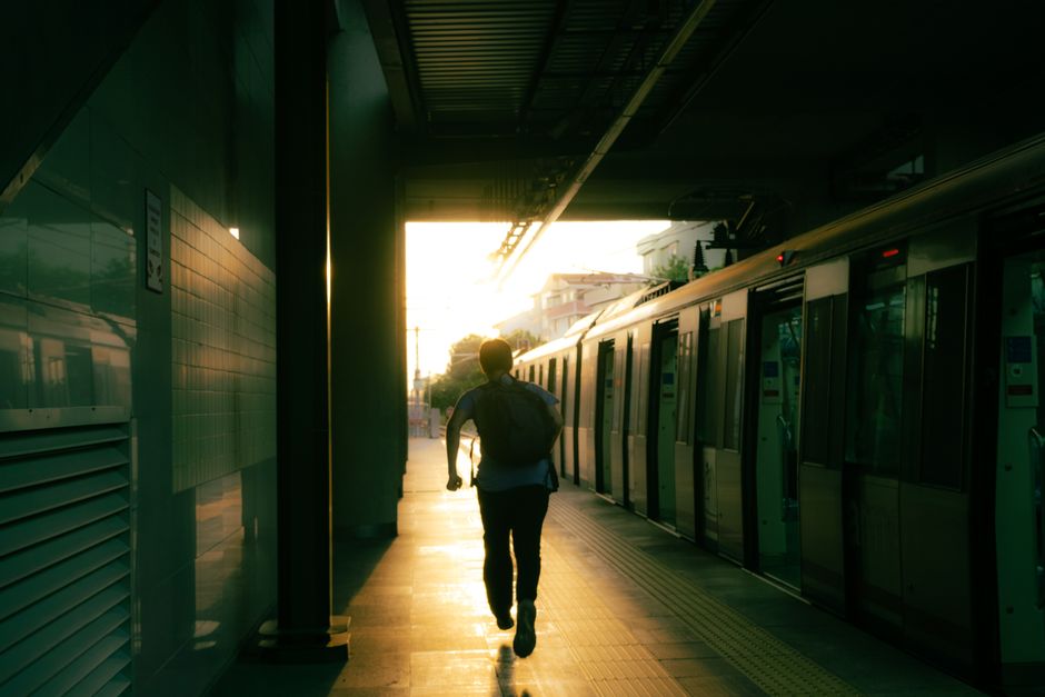 A man runs towards a departing train at sunset, captured in dim light at a train station.