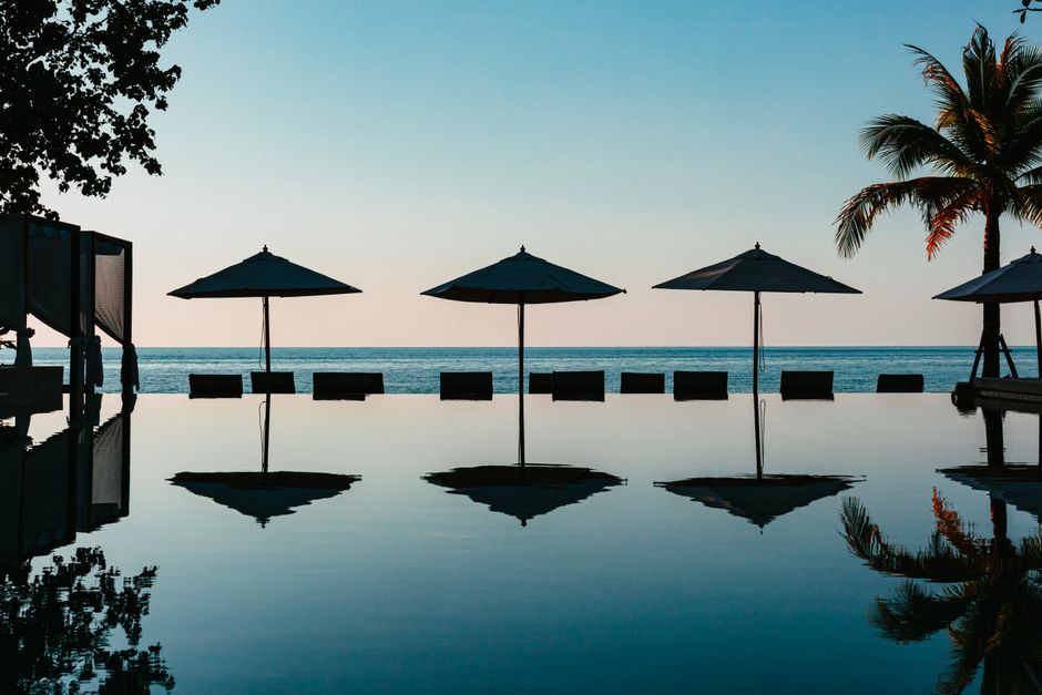Silhouette of tropical resort with sea view, palm trees, and sun loungers at sunset.